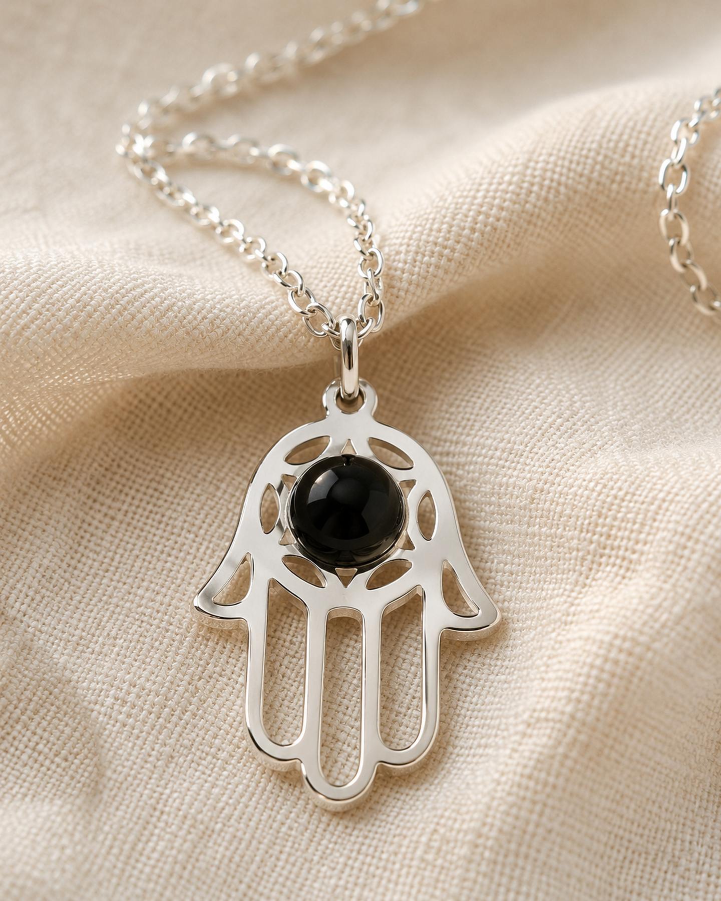 Detalle macro de la Mano de Luz (Hamsa) con su esfera de obsidiana negra brillante, sobre tela de lino crema