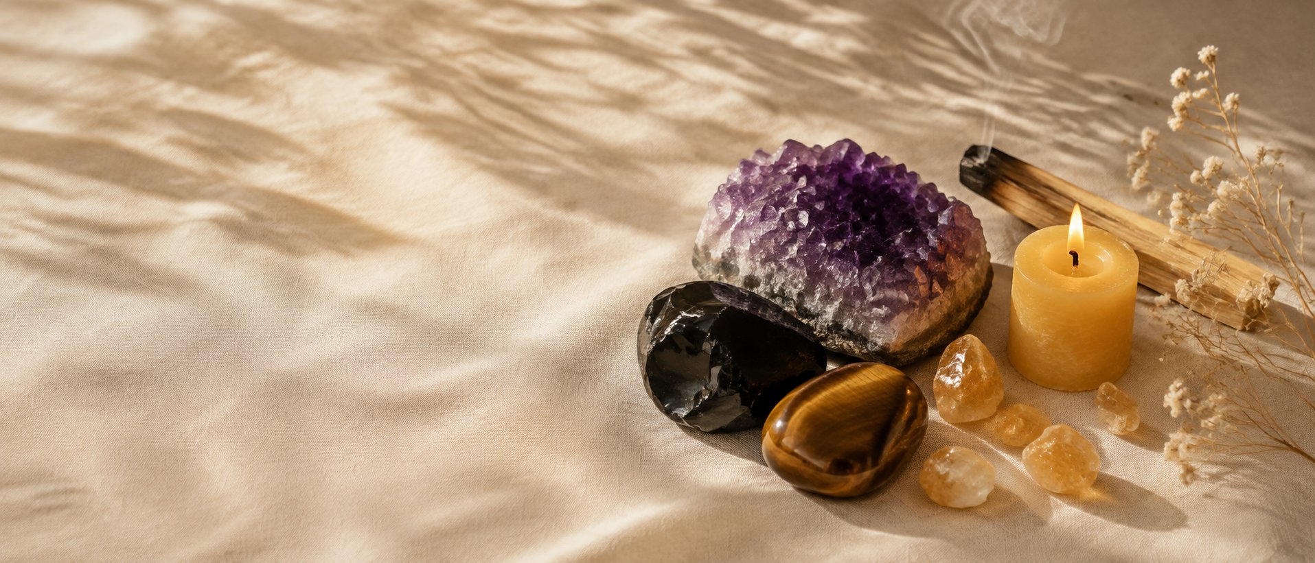 Bodegón de amuletos FENNTA: geoda de amatista, obsidiana, ojo de tigre y citrino con vela y palo santo sobre lino crema
