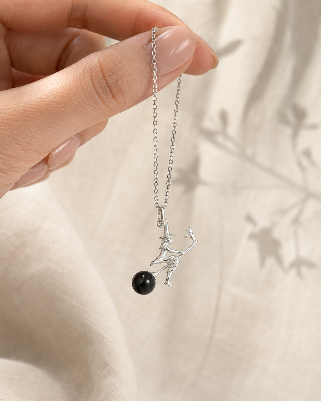 Mano sosteniendo el Colgante Brujita de plata 925 con esfera de obsidiana negra, sobre lino crema